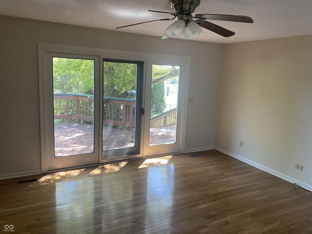 unfurnished room with a textured ceiling, a healthy amount of sunlight, ceiling fan, and dark hardwood / wood-style floors