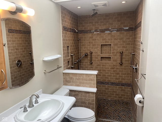 bathroom with toilet, a tile shower, and sink