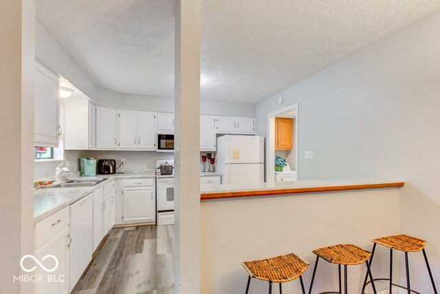 kitchen featuring kitchen peninsula, white cabinets, a kitchen bar, and white appliances