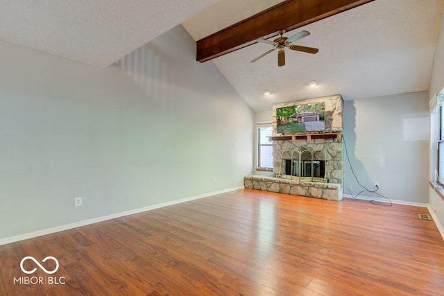 unfurnished living room featuring beamed ceiling, baseboards, a stone fireplace, and wood finished floors