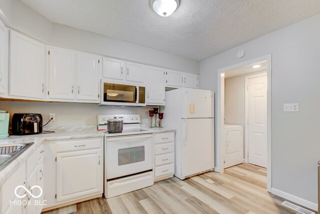 kitchen with white appliances, white cabinets, washer / dryer, and a textured ceiling