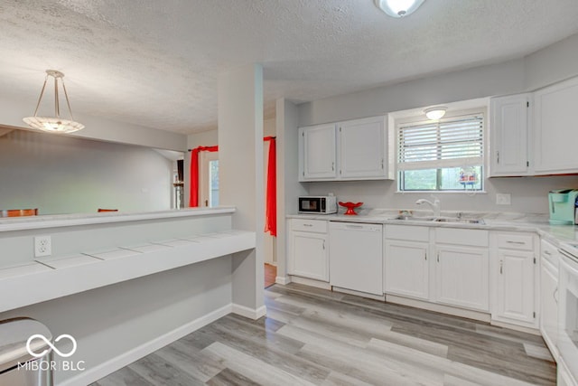 kitchen featuring pendant lighting, sink, white dishwasher, white cabinetry, and light wood-type flooring