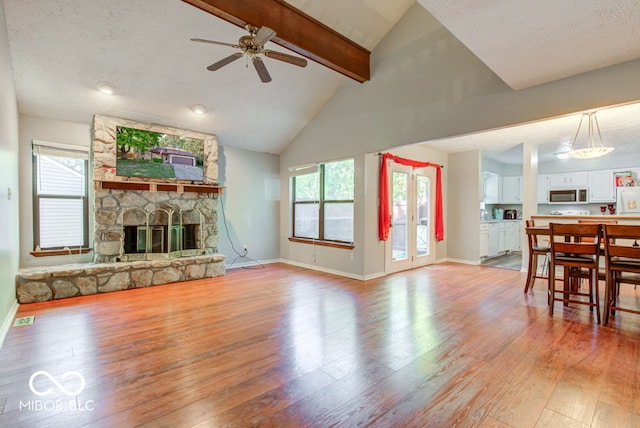 living area featuring a stone fireplace, beamed ceiling, visible vents, and light wood-type flooring