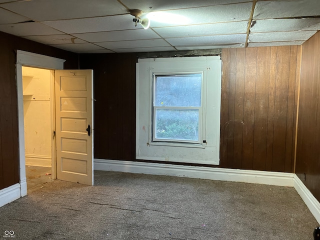 unfurnished room featuring wood walls, a drop ceiling, and carpet