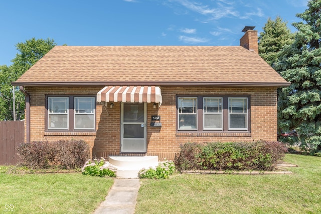 bungalow featuring a shingled roof, a front yard, brick siding, and a chimney