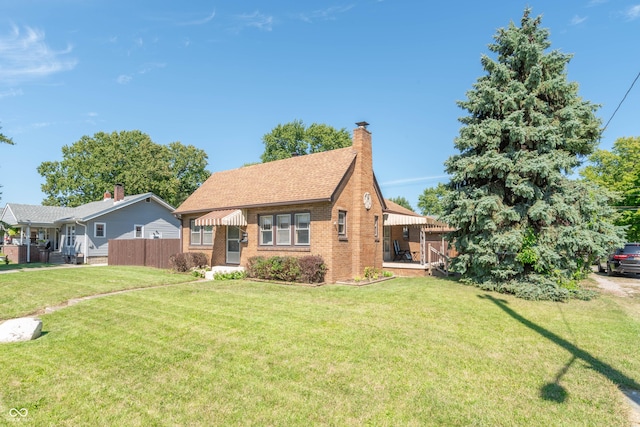 view of front facade featuring a front lawn, fence, roof with shingles, brick siding, and a chimney