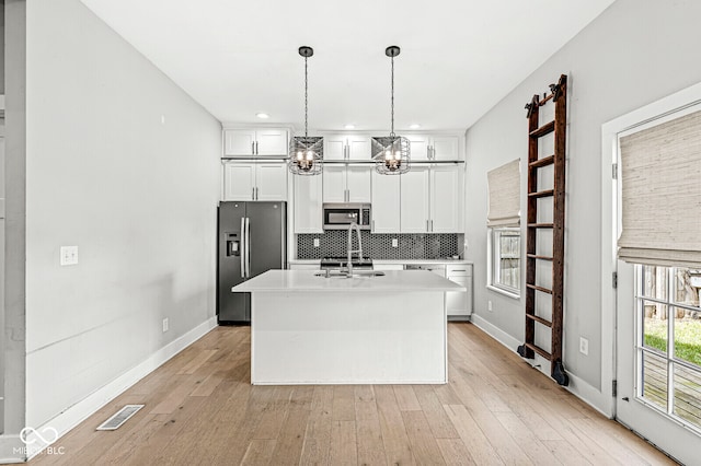 kitchen featuring light wood-type flooring, an island with sink, hanging light fixtures, appliances with stainless steel finishes, and white cabinets