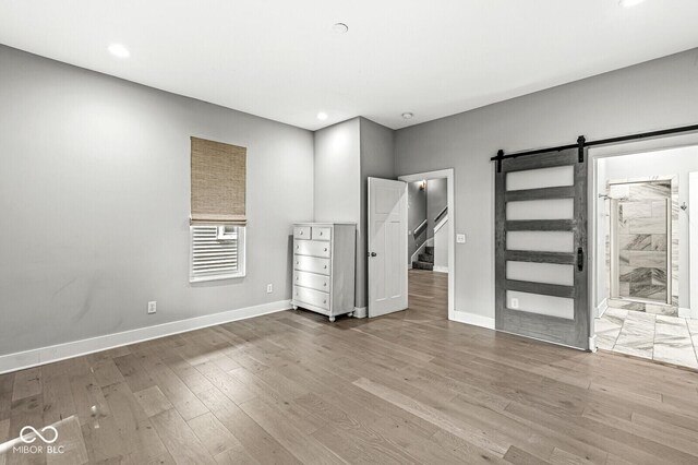 unfurnished bedroom featuring a barn door, connected bathroom, and light hardwood / wood-style floors