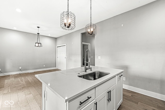 kitchen featuring pendant lighting, hardwood / wood-style floors, a kitchen island with sink, sink, and white cabinets