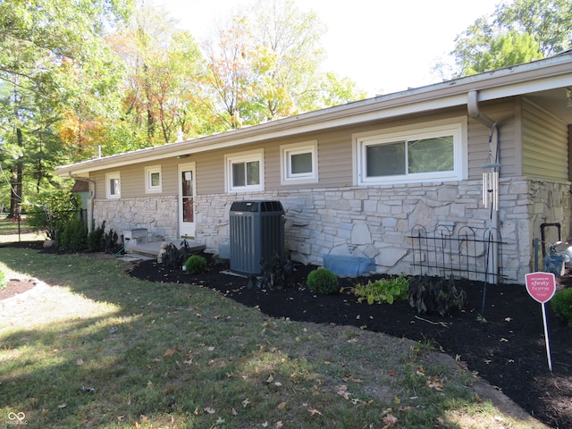 exterior space featuring cooling unit, stone siding, and a lawn