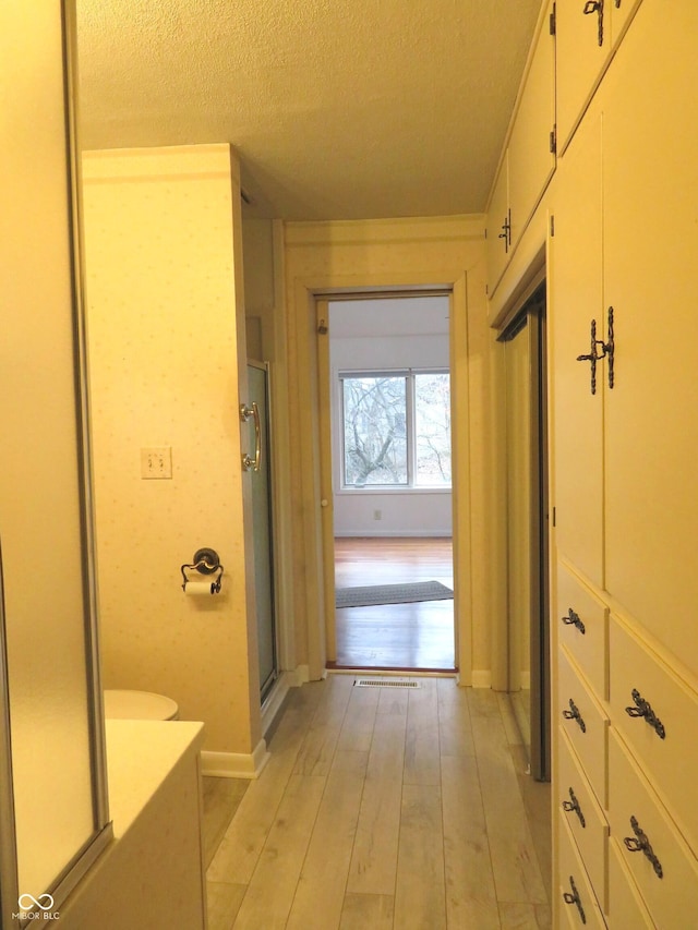 corridor with light hardwood / wood-style floors and a textured ceiling