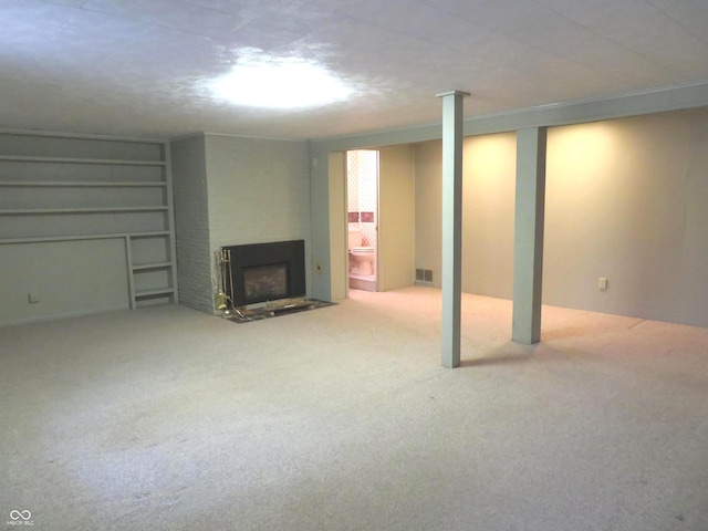 finished below grade area with visible vents, a fireplace with flush hearth, ornamental molding, built in features, and carpet flooring