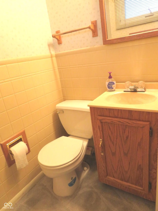 half bathroom featuring a wainscoted wall, toilet, vanity, and wallpapered walls