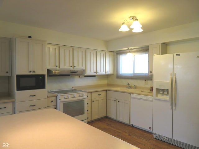 kitchen featuring a sink, under cabinet range hood, light countertops, white appliances, and dark wood-style flooring