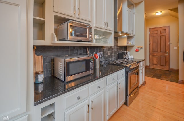 kitchen featuring appliances with stainless steel finishes, decorative backsplash, white cabinetry, light wood-type flooring, and dark stone counters