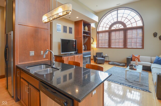 kitchen with stainless steel appliances, a center island with sink, sink, and light hardwood / wood-style floors