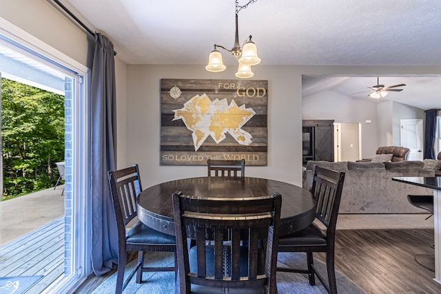 dining room featuring ceiling fan with notable chandelier, vaulted ceiling, a textured ceiling, and dark hardwood / wood-style floors