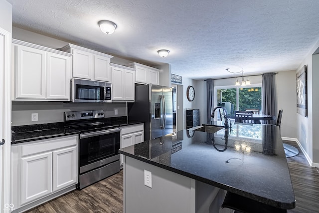 kitchen with stainless steel appliances, a sink, white cabinetry, dark wood-style floors, and an island with sink