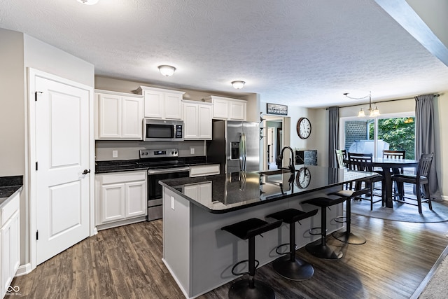 kitchen with an island with sink, dark hardwood / wood-style floors, stainless steel appliances, and white cabinets