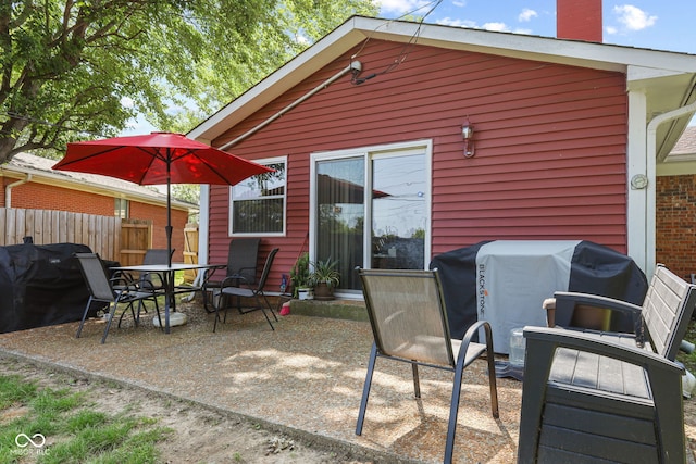 back of house with outdoor dining space, a patio area, fence, and a chimney