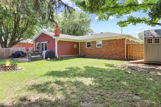 back of house featuring a fenced backyard, a chimney, a fire pit, and brick siding