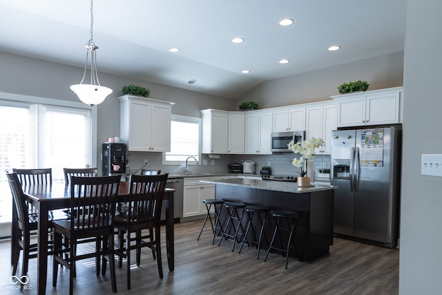 kitchen with a kitchen island, vaulted ceiling, dark wood-type flooring, stainless steel appliances, and white cabinets