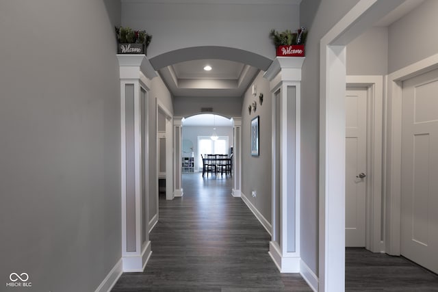 hall featuring dark wood-type flooring, a tray ceiling, and decorative columns