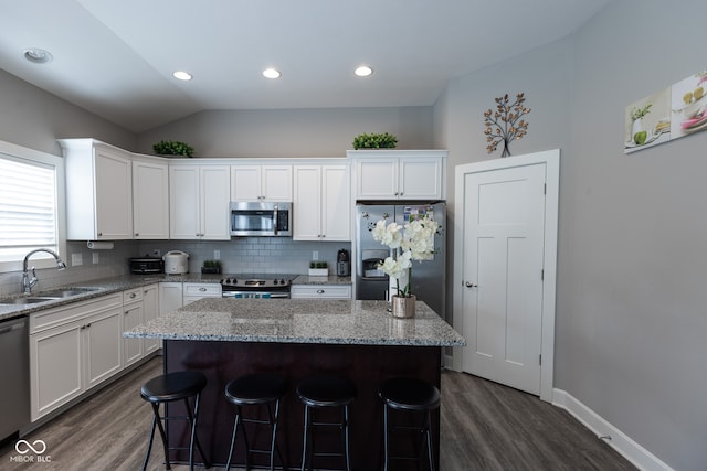 kitchen featuring appliances with stainless steel finishes, vaulted ceiling, a center island, and sink