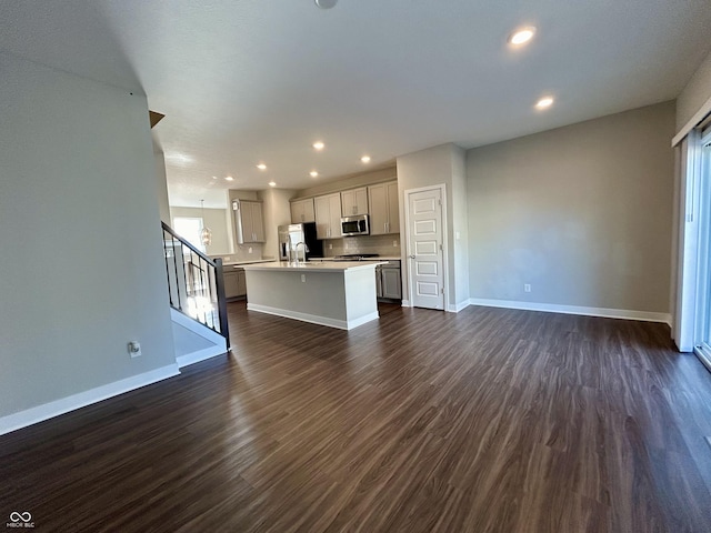 kitchen with a kitchen island with sink, dark wood-type flooring, white cabinets, decorative backsplash, and appliances with stainless steel finishes