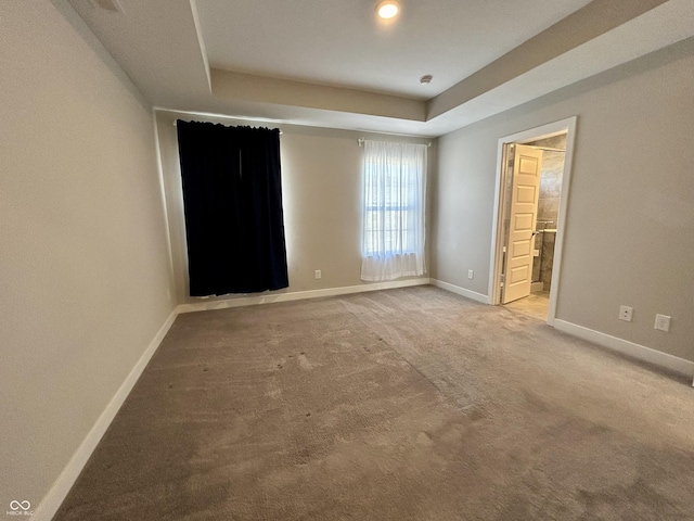 unfurnished bedroom featuring light carpet, connected bathroom, and a tray ceiling