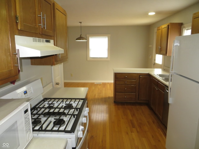 kitchen featuring hanging light fixtures, kitchen peninsula, white appliances, and light hardwood / wood-style floors