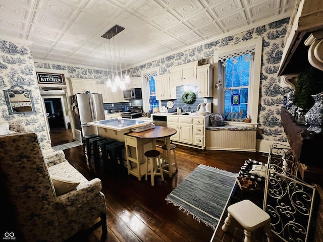 kitchen with a kitchen island, wallpapered walls, appliances with stainless steel finishes, dark wood-style floors, and an ornate ceiling