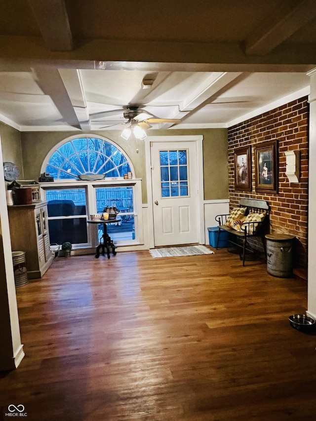 foyer entrance featuring beamed ceiling, a wainscoted wall, a ceiling fan, wood finished floors, and brick wall