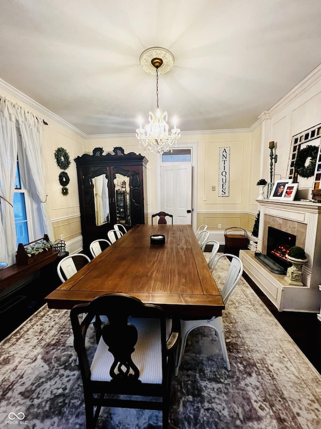 dining space featuring a notable chandelier, a decorative wall, crown molding, and a premium fireplace