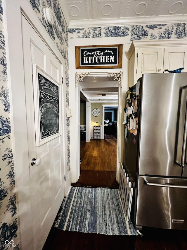 kitchen with wallpapered walls, dark wood-type flooring, ornamental molding, freestanding refrigerator, and cream cabinetry