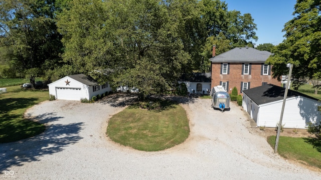 colonial-style house with a garage, an outbuilding, gravel driveway, and a front yard