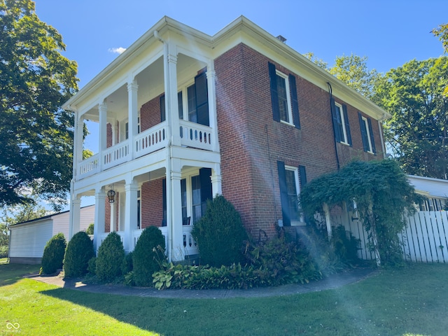 view of side of property with brick siding, fence, a porch, a lawn, and a balcony