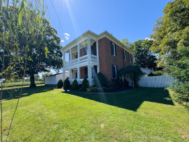 view of side of home with a yard, brick siding, a balcony, and fence