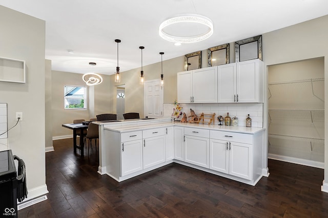 kitchen featuring a peninsula, decorative backsplash, light countertops, dark wood-type flooring, and white cabinetry