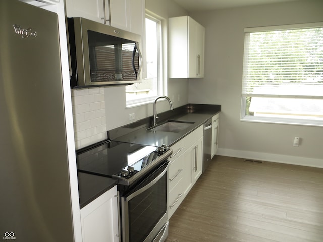 kitchen with backsplash, light hardwood / wood-style flooring, appliances with stainless steel finishes, white cabinetry, and sink