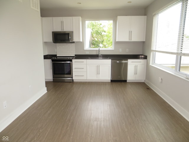 kitchen with appliances with stainless steel finishes, plenty of natural light, wood-type flooring, and white cabinetry