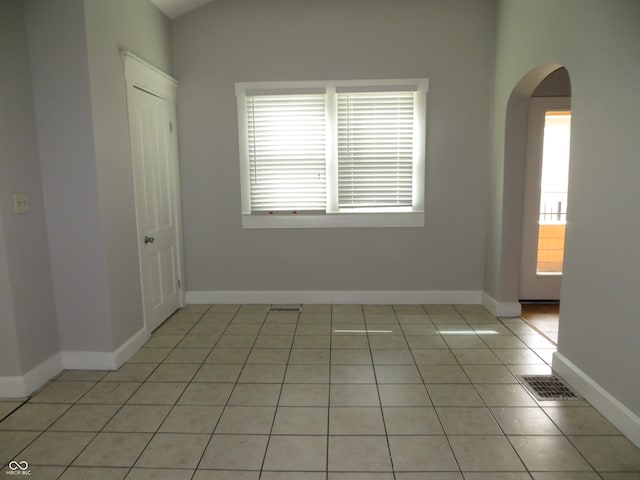 tiled empty room featuring lofted ceiling