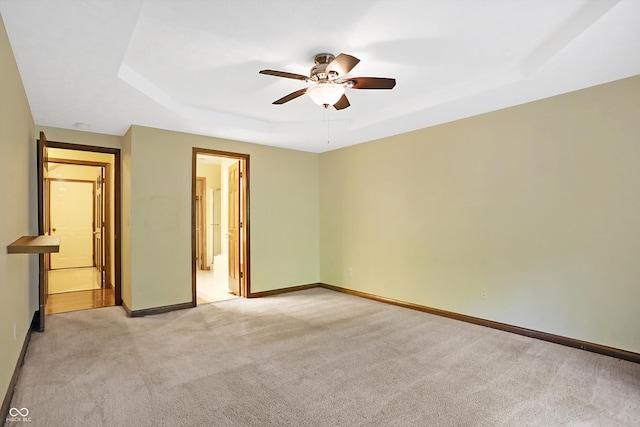 unfurnished bedroom with ceiling fan, a raised ceiling, light colored carpet, and ensuite bath