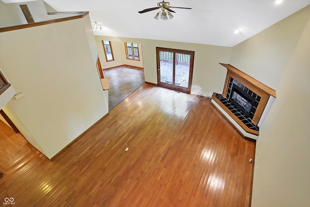 unfurnished living room with a tiled fireplace, ceiling fan, and wood-type flooring