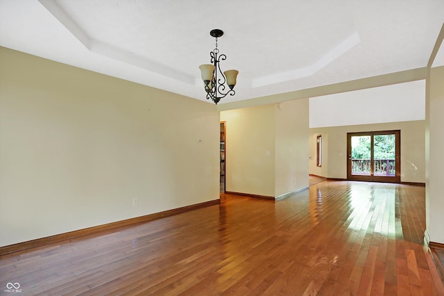 spare room with hardwood / wood-style flooring, a notable chandelier, and a tray ceiling