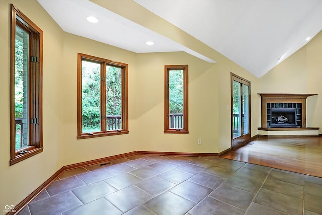 unfurnished living room featuring dark tile patterned flooring, lofted ceiling, and a fireplace