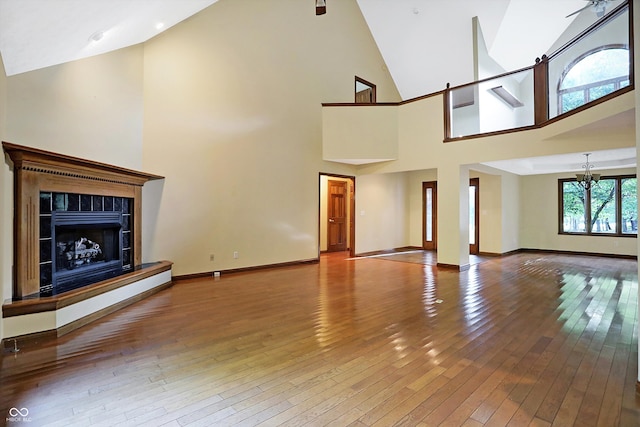 unfurnished living room with a chandelier, hardwood / wood-style flooring, high vaulted ceiling, and a tiled fireplace