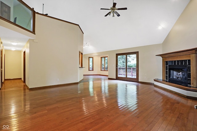 unfurnished living room with hardwood / wood-style flooring, ceiling fan, a tile fireplace, and high vaulted ceiling