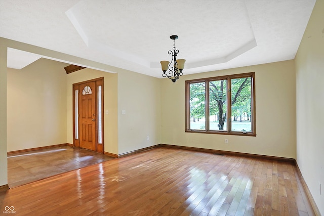 spare room with hardwood / wood-style flooring, a raised ceiling, a textured ceiling, and a chandelier