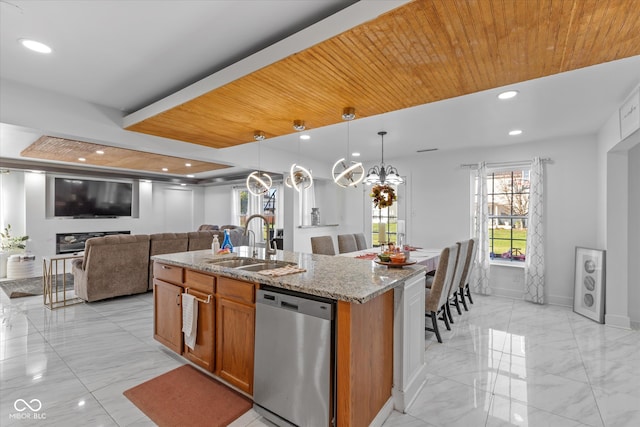 kitchen with light stone countertops, sink, stainless steel dishwasher, an island with sink, and pendant lighting